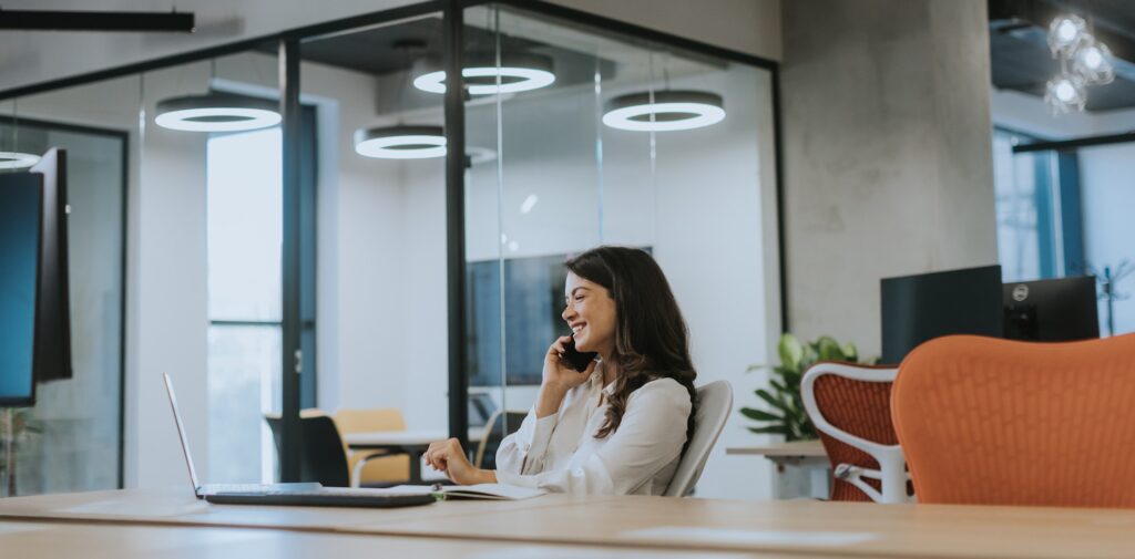 Young business woman using mobile phone while working on laptop in the modern office